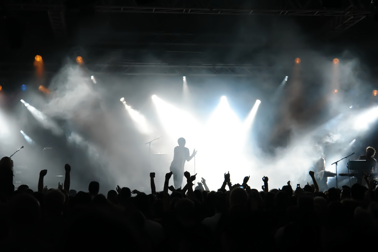 Man on stage with concert crowd below and bright spotlights